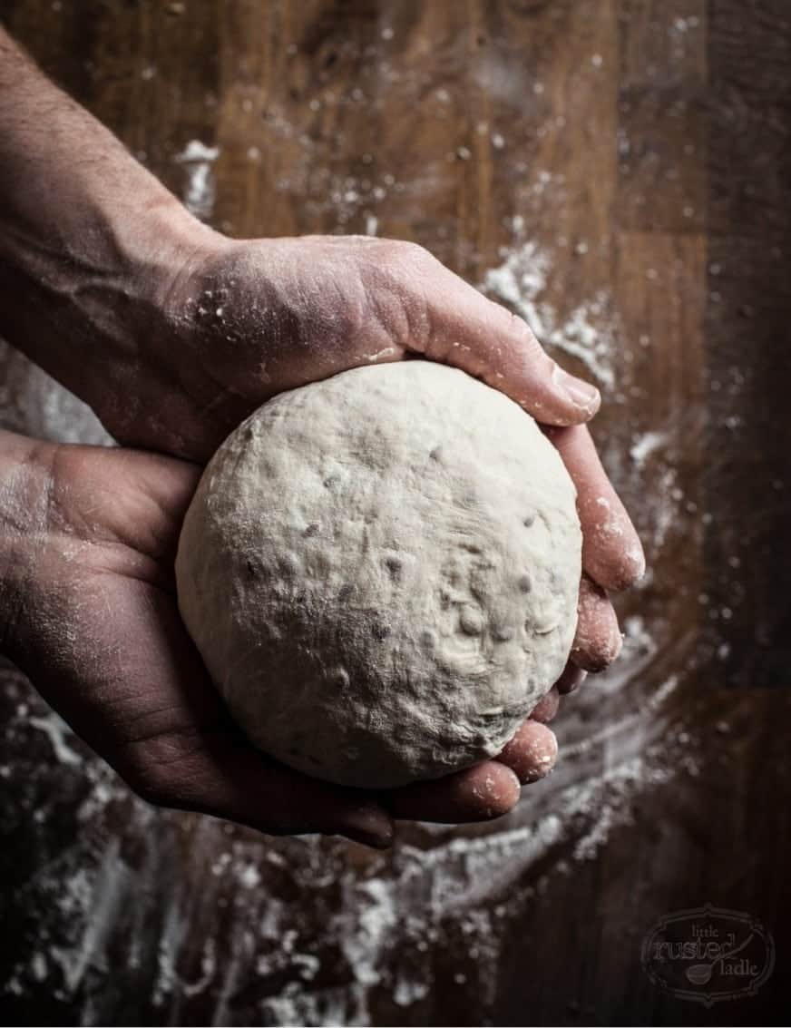 Hands covered in flour holding a ball of bread dough. Hands make an Instagram food picture more relatable. 