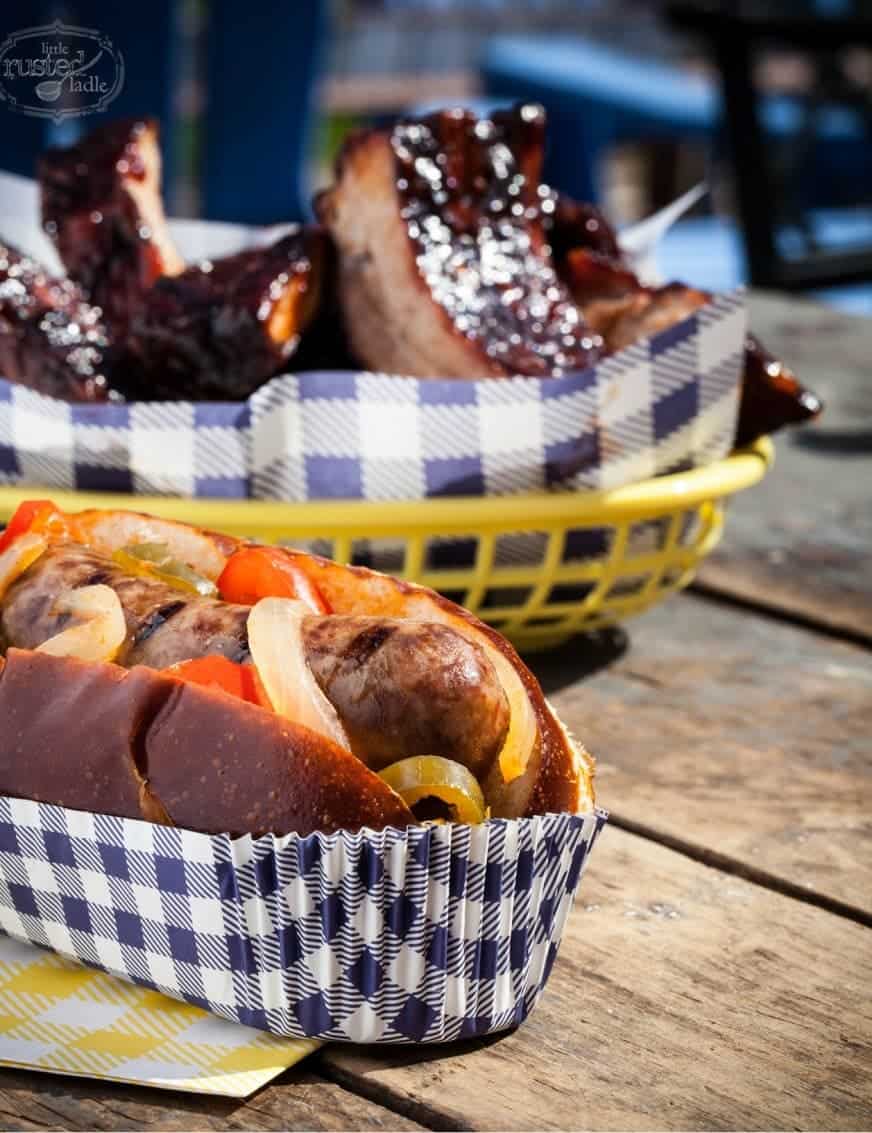 Outdoor picture of a brat and BBQ ribs in food baskets with checkered paper. Display taking a photo quickly so food looks good. 