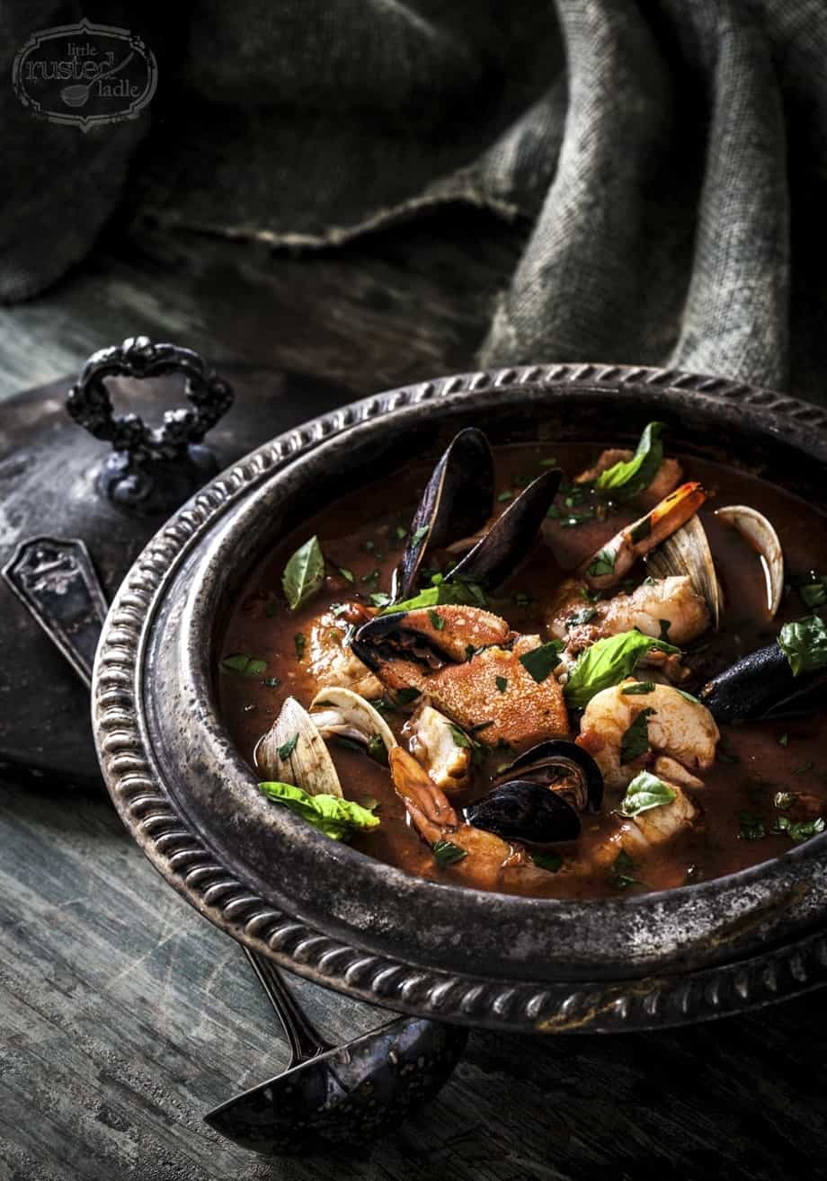 Cioppino Seafood Stew Soup in dark metal pot on gray wood surface.