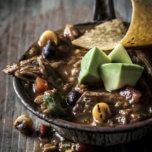 Pork and Pumpkin Mole Chili in a metal tin with a long handle in a dark setting