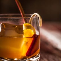 Tub glass with amber cocktail garnished with lemon, strawberry, and rhubarb.