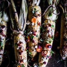 Cobs of corn with the husks pulled up colored with spices and peppers. Dark photography.