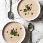 Look down on two white bowls of soup diagonal with spoons to the side.