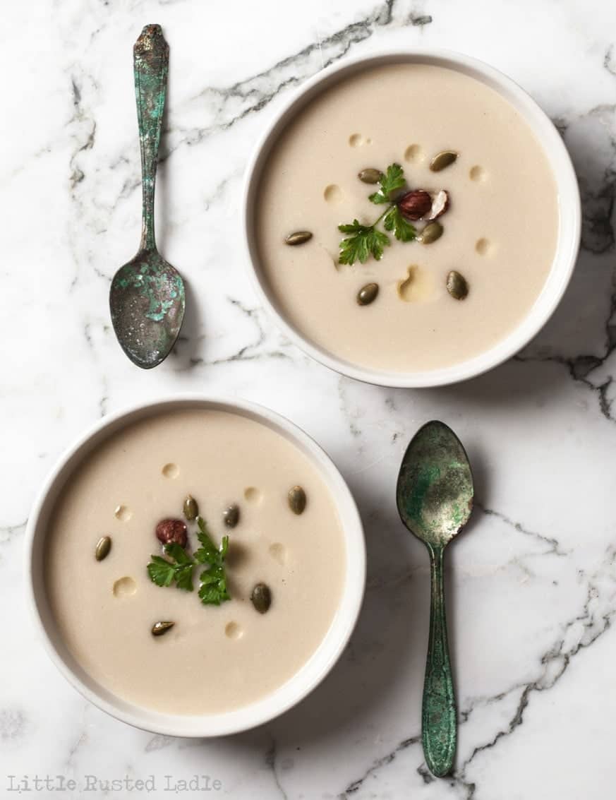 Look down on two white bowls of soup diagonal with spoons to the side. On white marble food background