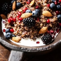 Closeup of rustic bowl containing fresh fruit, milk, nuts, and quinoa