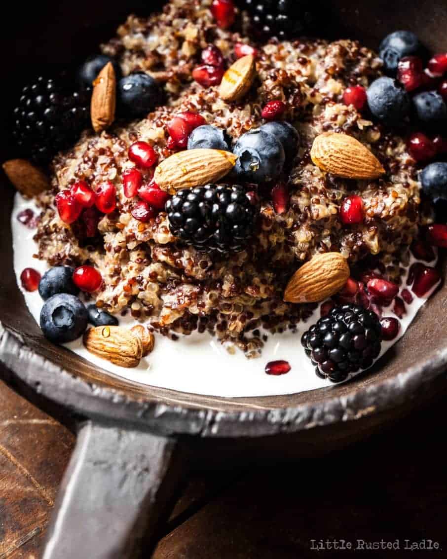 Closeup of rustic bowl containing fresh fruit, milk, nuts, and quinoa