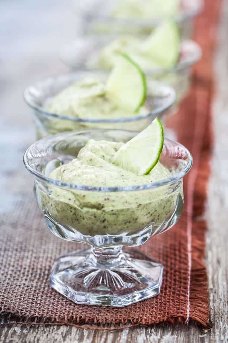 A receding line of crystal ice cream dishes filled with light green key lime pudding on rustic table runner.