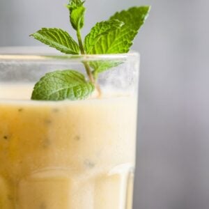 Close up of drinking glass filled with yellow smoothie with mint garnish