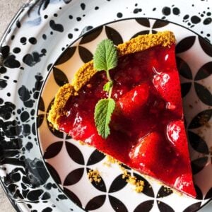 A piece of bright red strawberry pie on patterned black and white dishware.