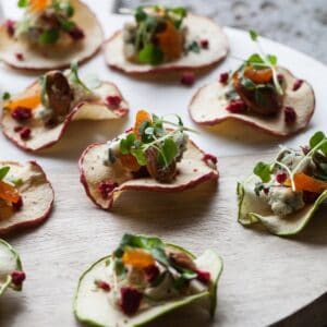 Wood platter of dried apple crisps topped with cheese fruit and nuts