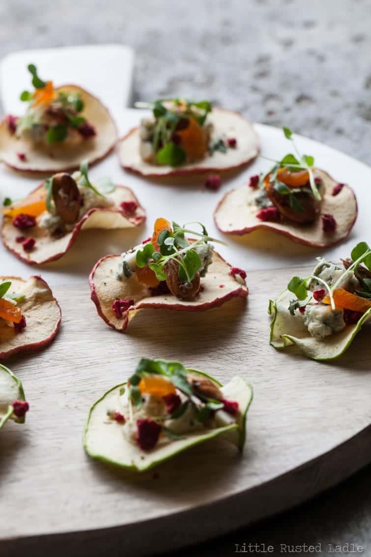 Wood platter of dried apple crisps topped with cheese fruit and nuts