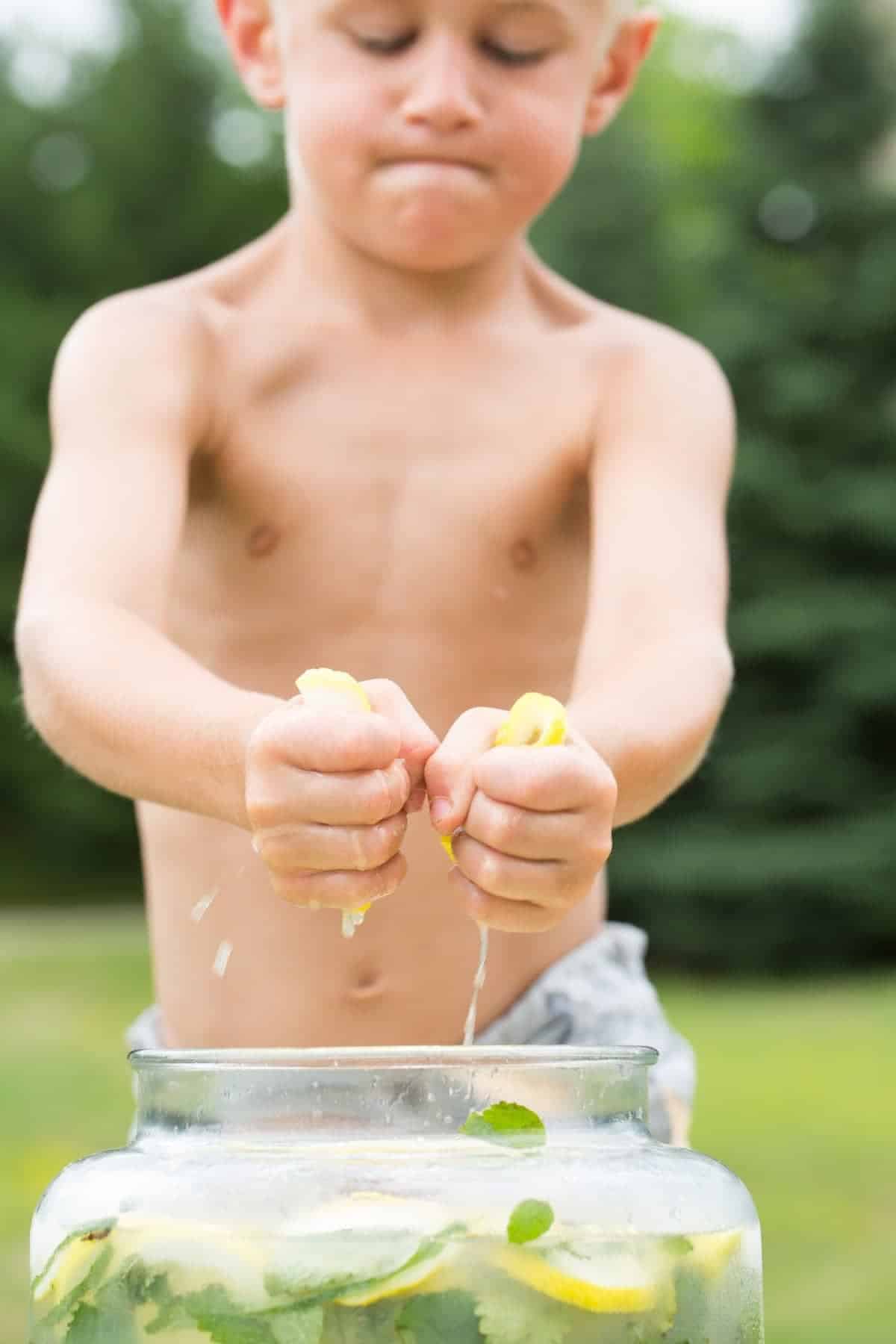 Little boy squeezing lemons into a beverage jug. 