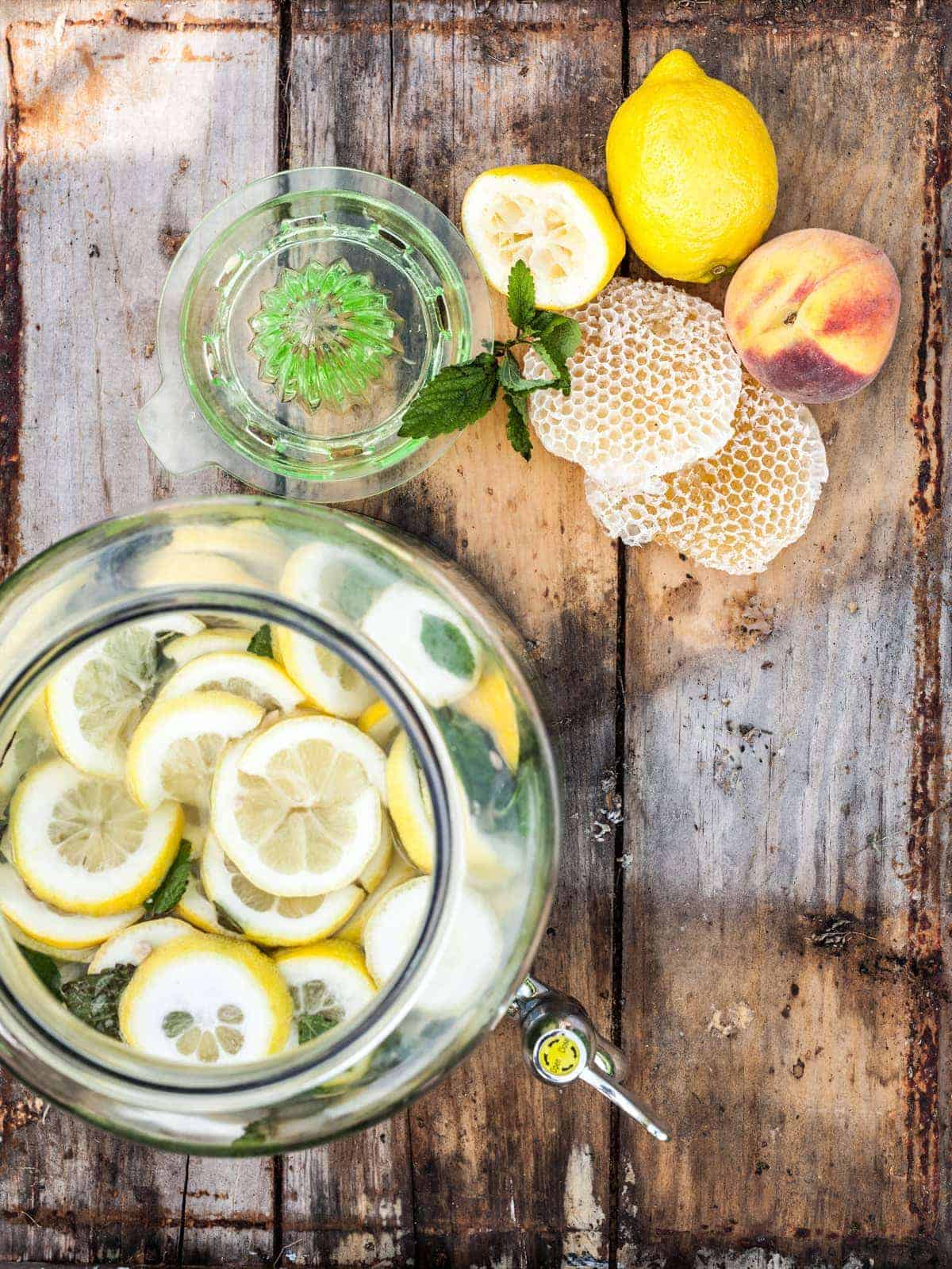 Drink jug full of lemonade from above with lemons, peach, and honeycomb to the side