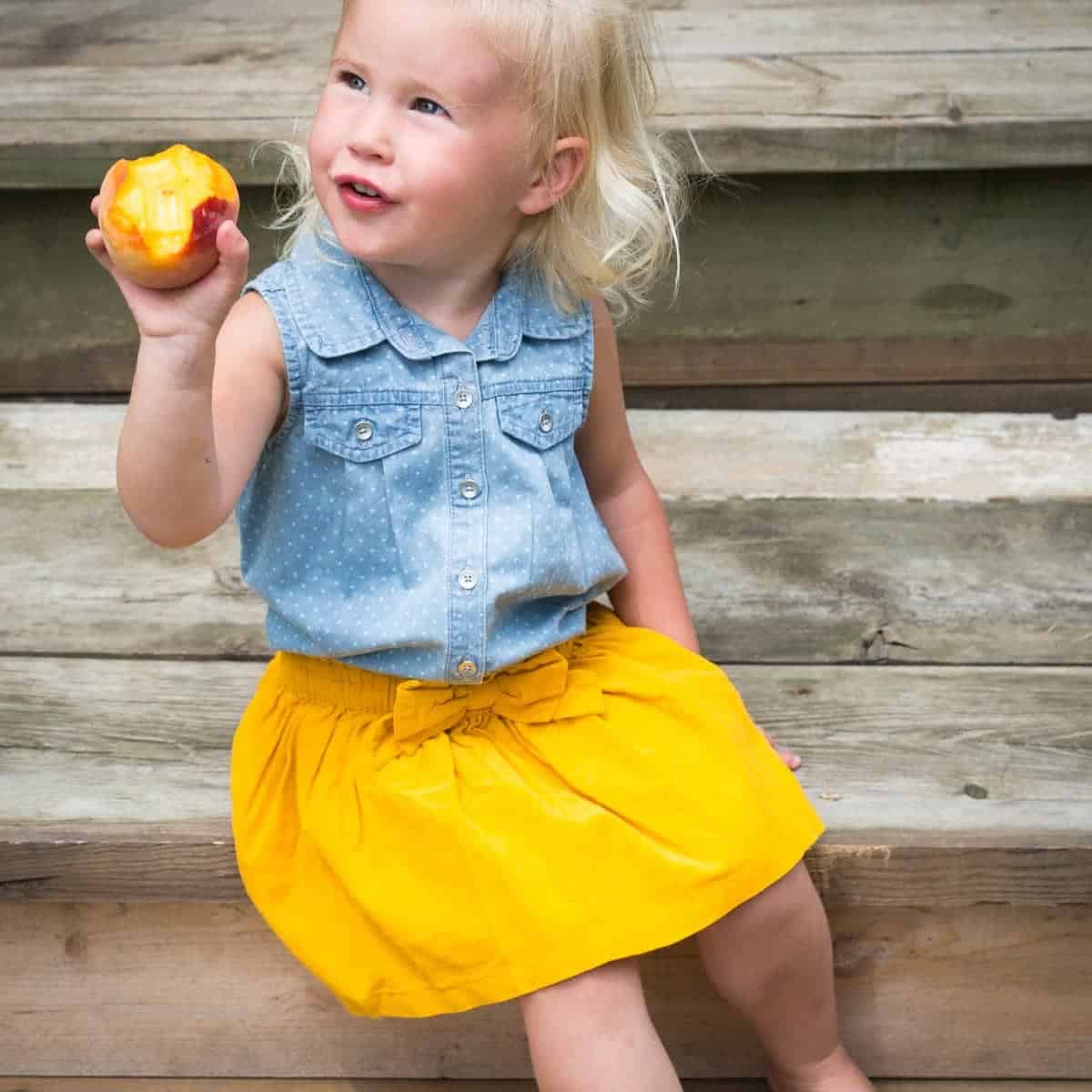 Little girl in yellow skirt eating a peach