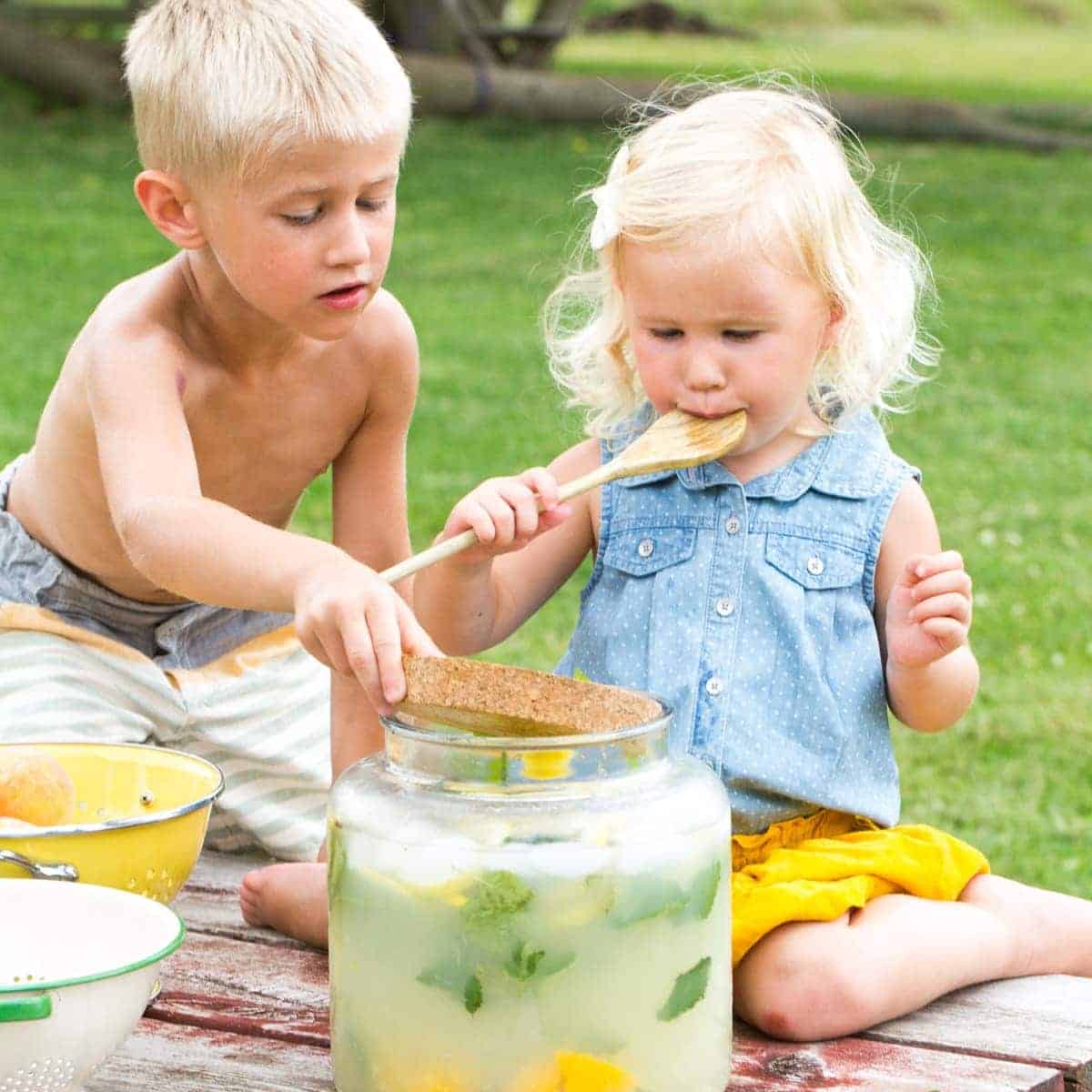 siblings making lemonade and licking the spoon