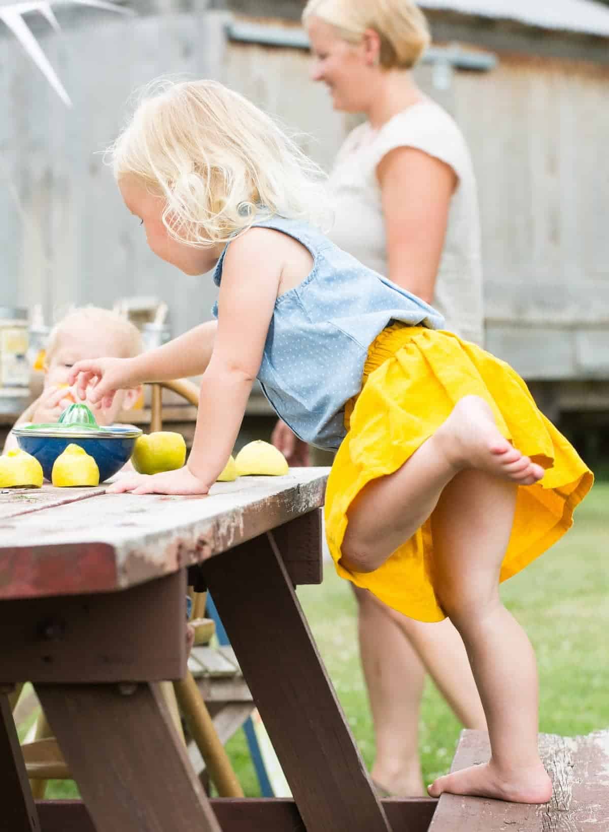 Little girl in a yellow skirt juicing lemons on a picnic table. 