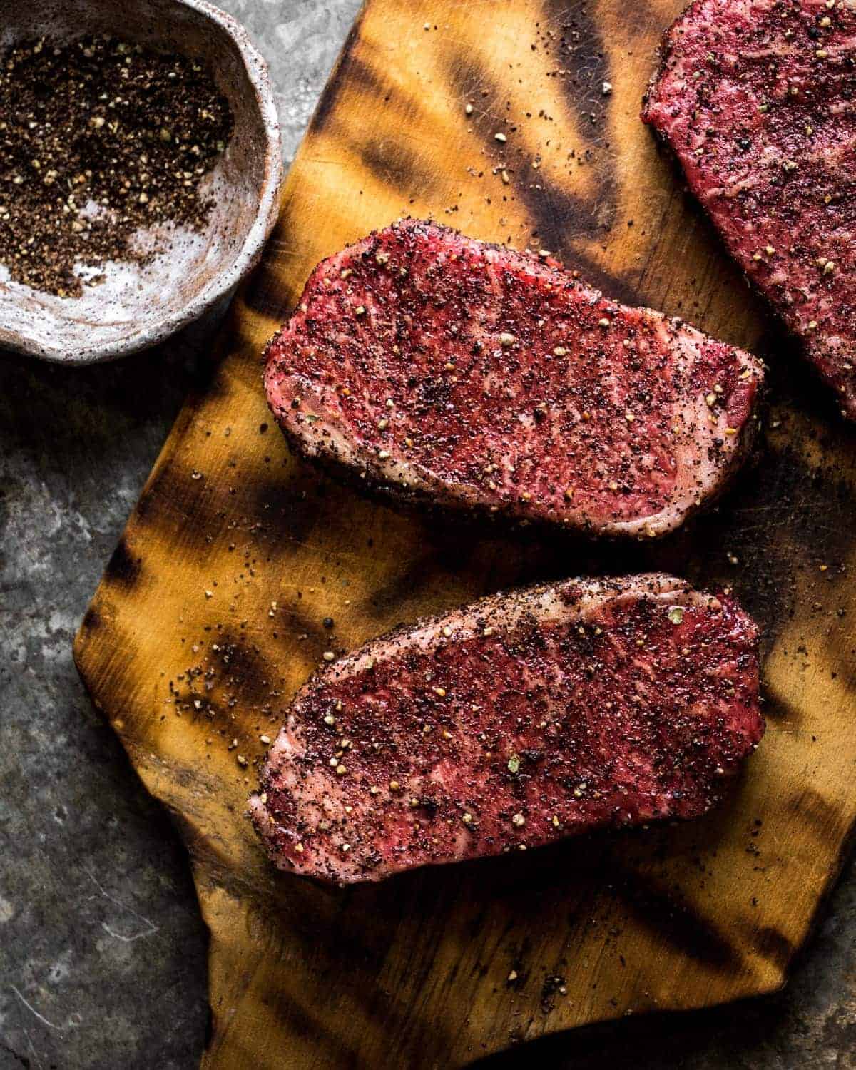 strip steaks covered in coffee seasoning mix resting on a vintage wooden cutting board. 