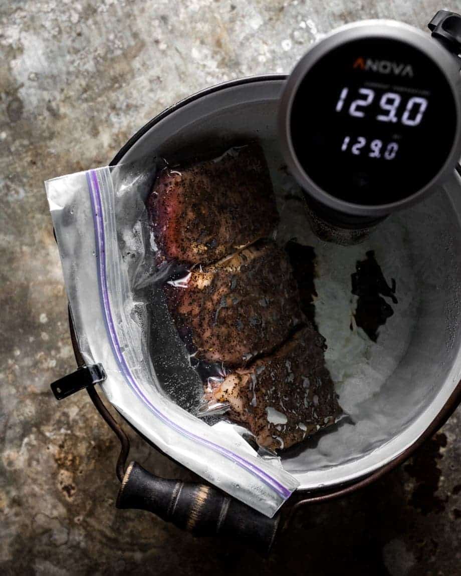 Process shot of three steaks in a resealable bag in a bucket with the sous vide cooker set to 129 degrees 