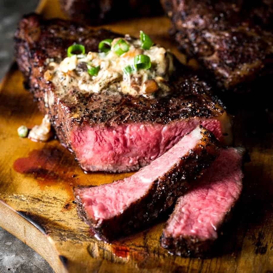 Close up of sliced sous vide strip steak with a warm pink center. Topped with smoky blue cheese butter