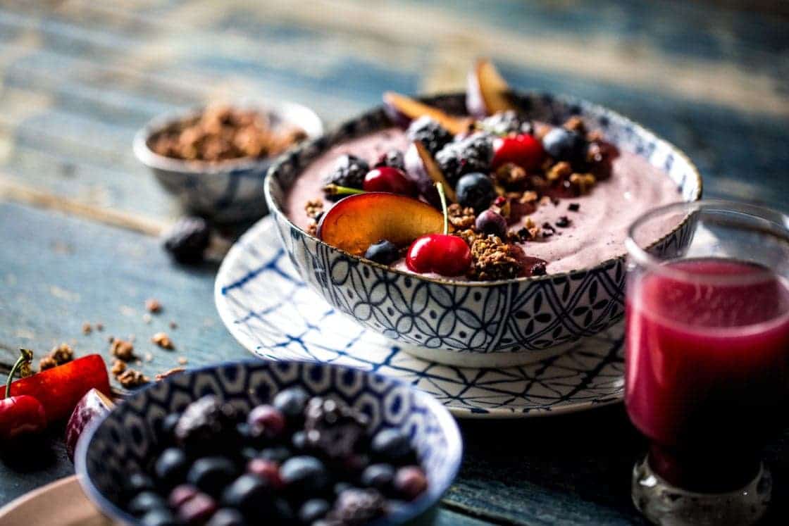 cherry smoothie bowl with a glass of juice and granola