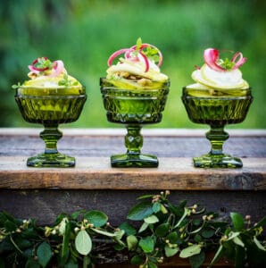 Three vintage green glass goblets on a rustic outdoor surface with light pear and rhubarb salad
