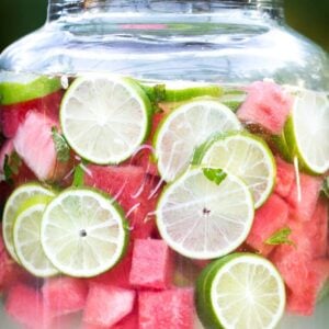 Large beverage container with fresh limes and watermelon pieces floating in limeade