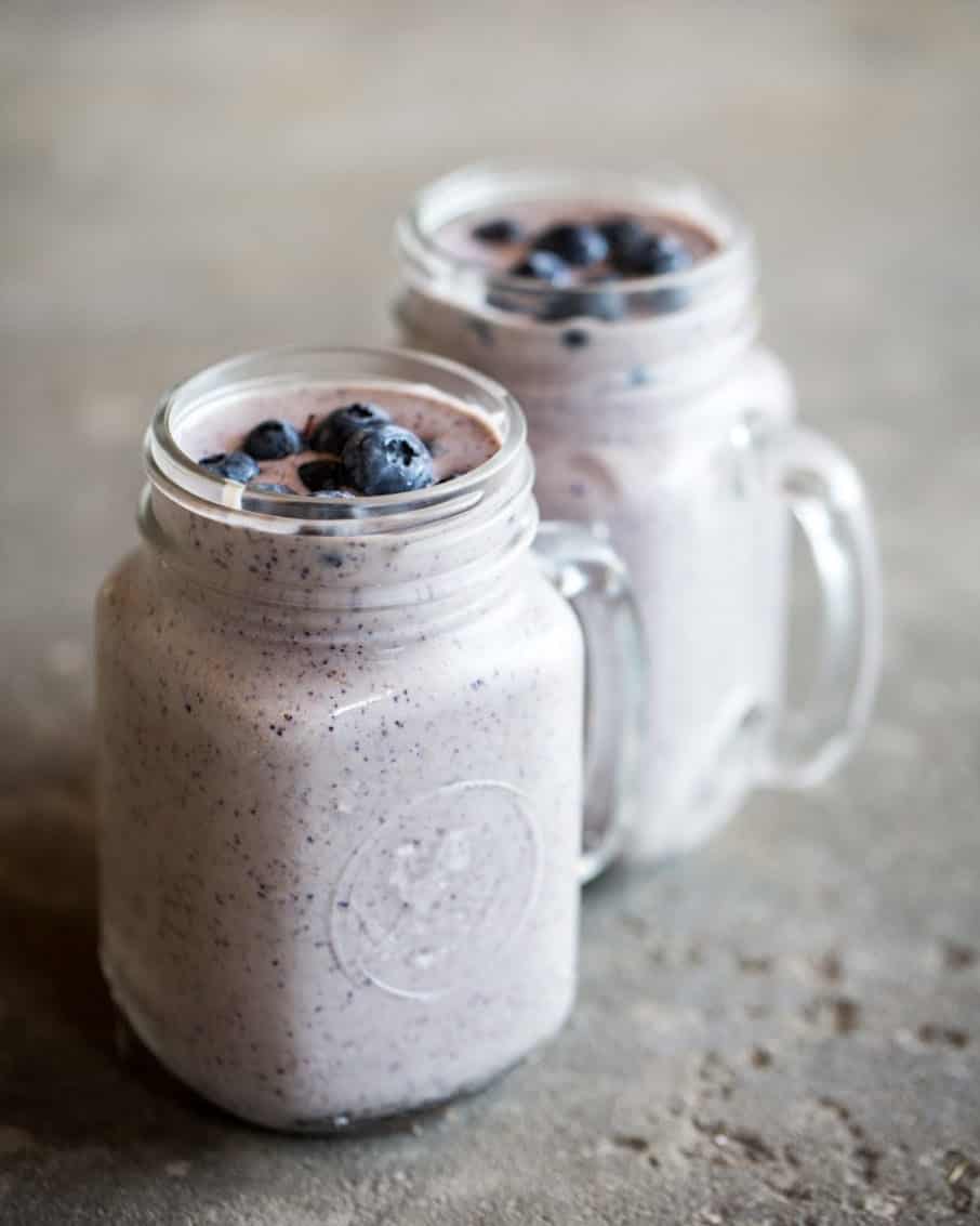 Two mason jar mugs filled with a creamy smoothie topped with fresh blueberries