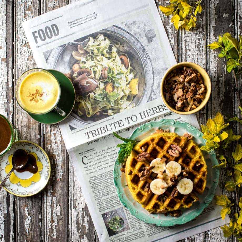 Table spread with waffles, granola, a latte and a newspaper. Showing how to take a good food photo for Instagram. 