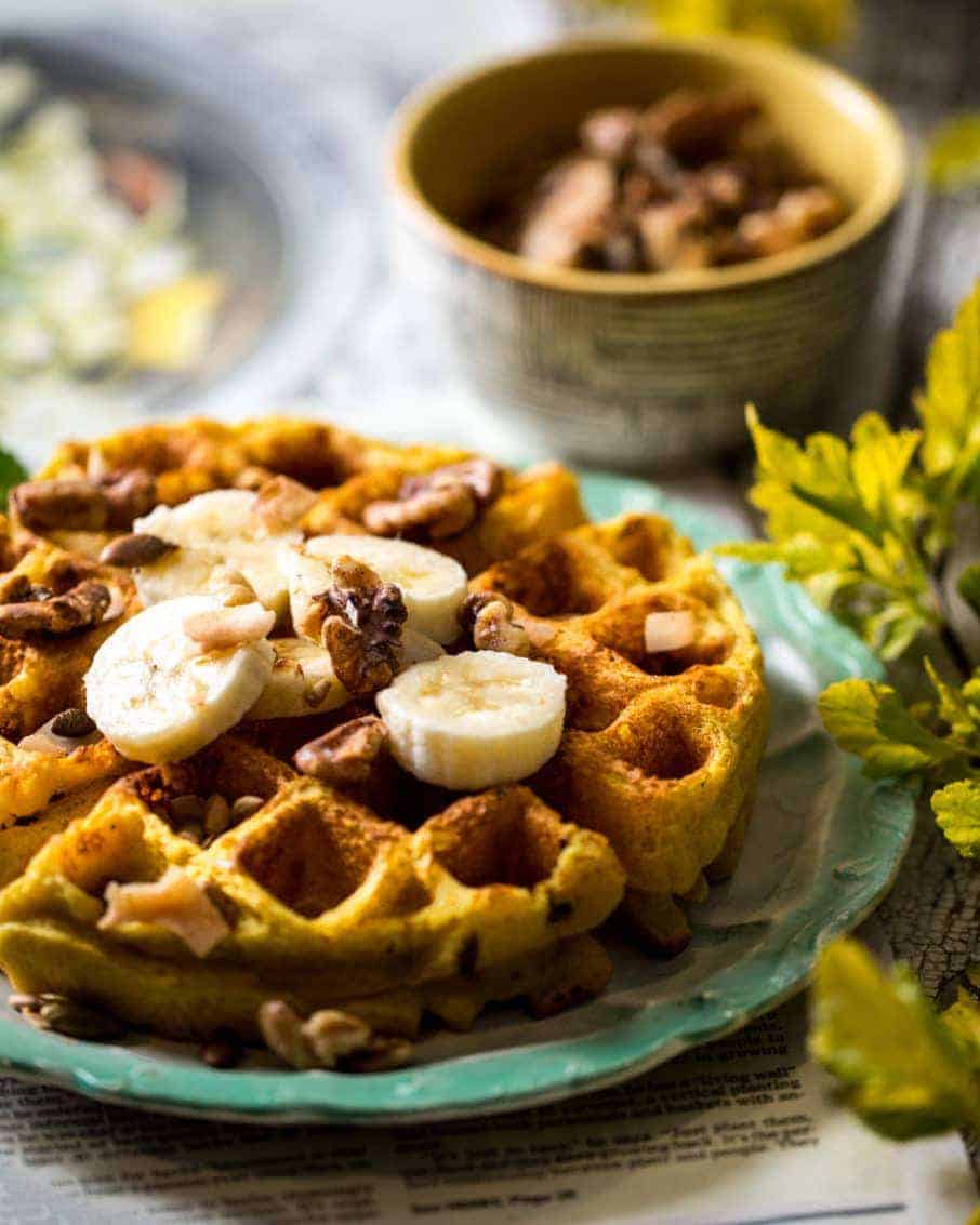 3/4 shot of big fluffy waffle with sliced bananas, chopped nuts, and chocolate