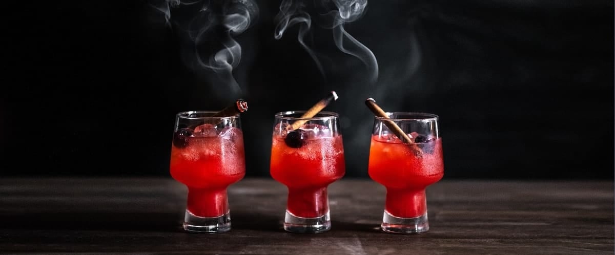 Three glasses of Candy Apple Old Fashioned with smoking cinnamon sticks. .