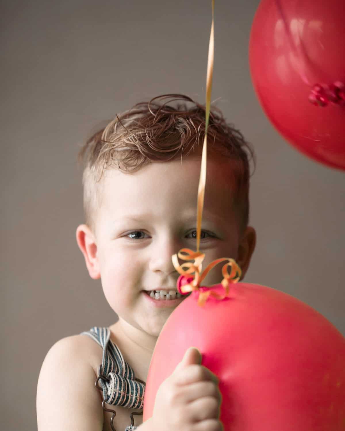 Austin smiling in overalls with red balloon