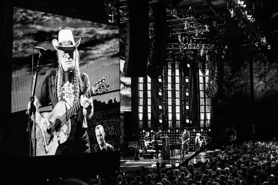 Distant shot of the Farm Aid stage with Willy Nelson on a video screen in the foreground. 