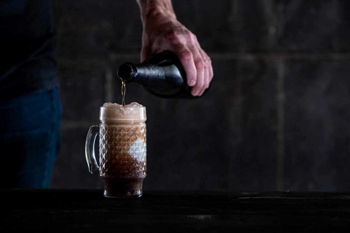 A man pouring a beer into a frothy glass mug. 