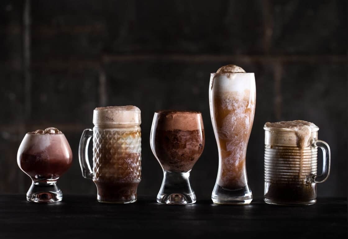 Commercial photography of a line of fun glassware filled with creamy beer floats against a dark background