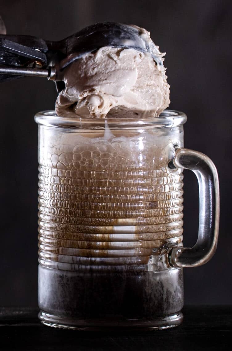 Hand scooping ice cream into a frosty mug of beer.