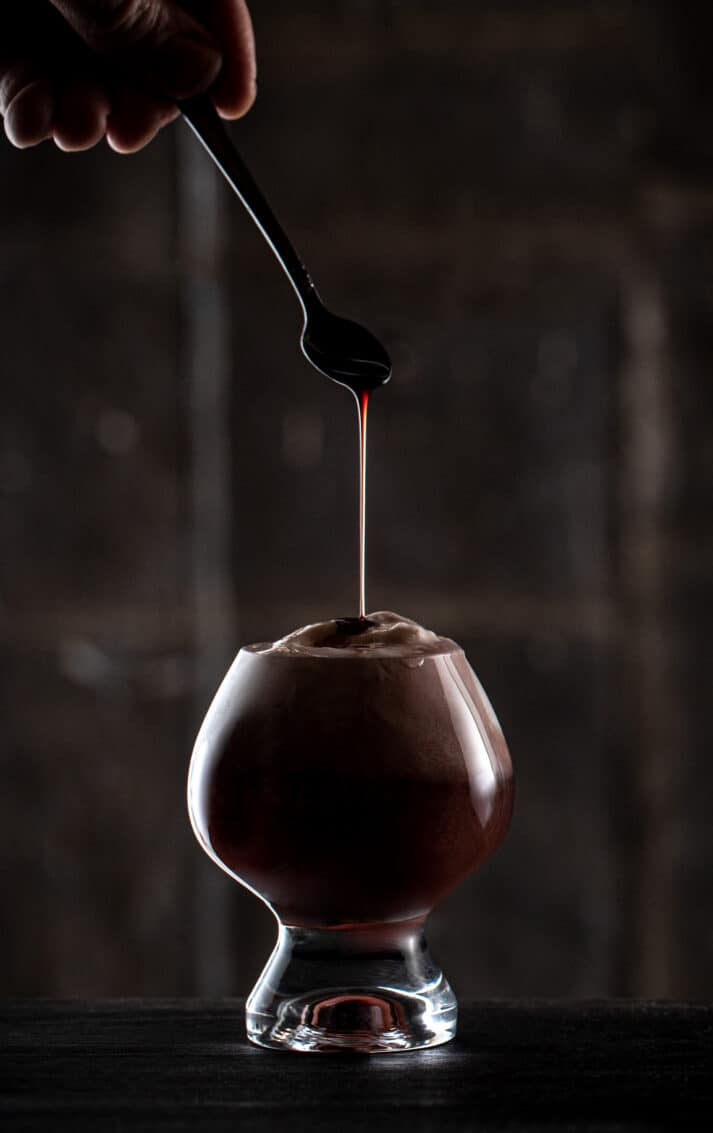 Dark drink photography with a spoon dripping syrup into a glass with dramatic lighting. Don't use your flash, use an alternate light source. 