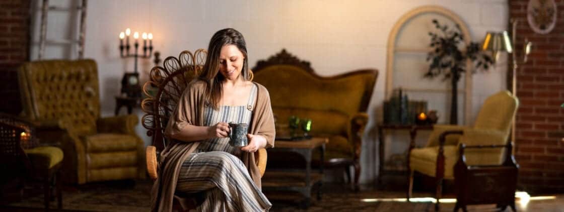 Lifestyle branding image of a woman photographer in her warm, Rustic, and inviting studio drinking coffee.