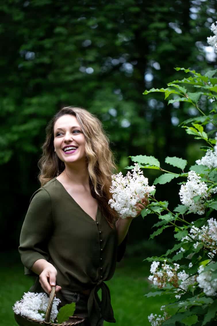 Woman picking white lilacs smiling with a brass basket