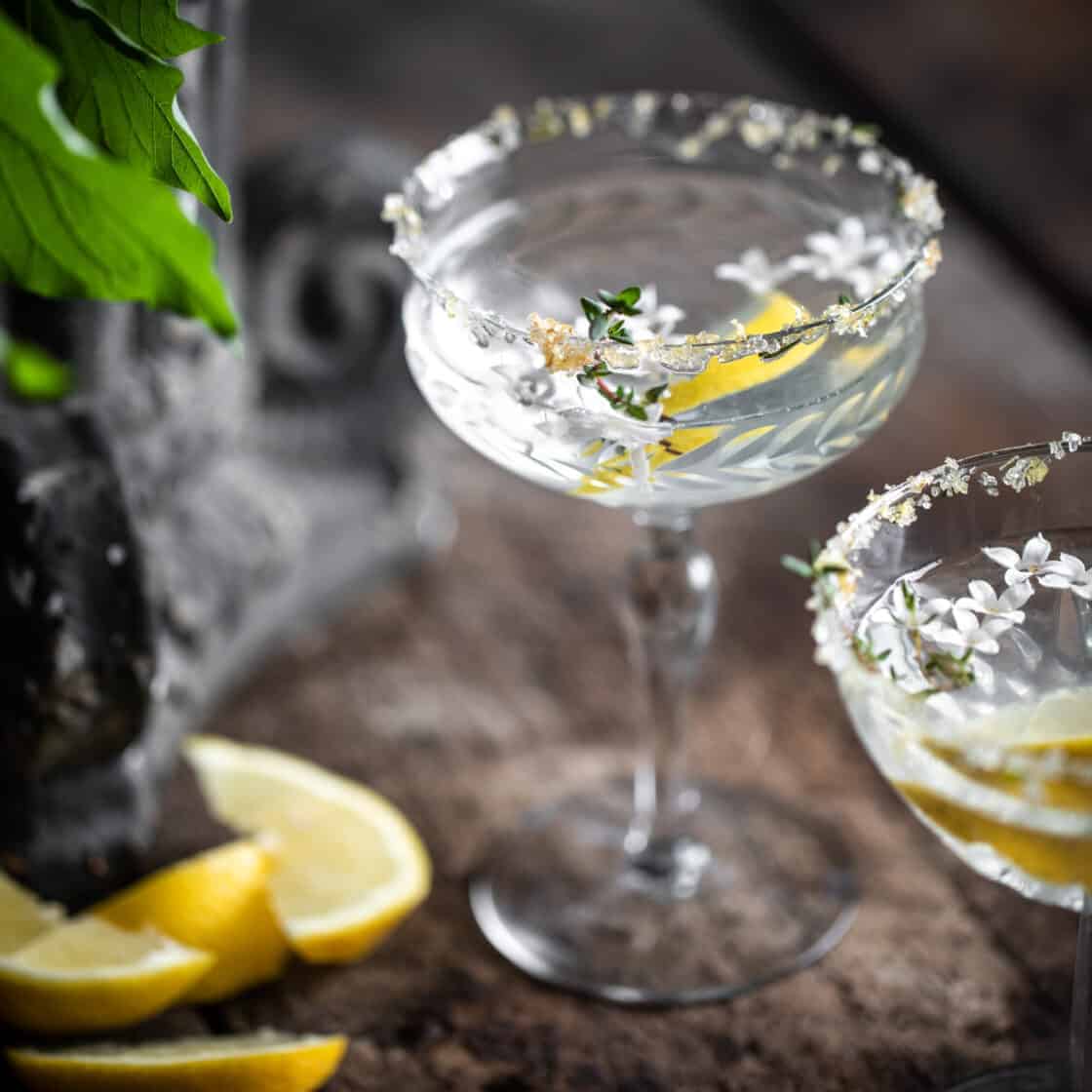 Lemon drop martini in rustic setting with thyme lemon zest and lilac on the rim of the glass 3/4 view of garnished drink photography