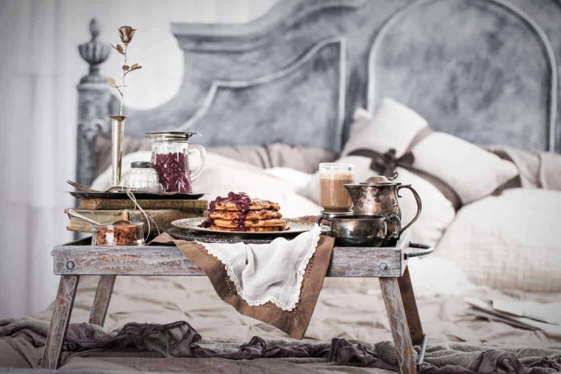 breakfast in bed with pancakes, maple coffee and blueberry syrup in a gray and white bedroom on wooden tray