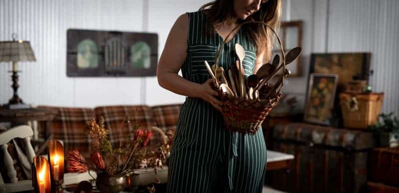 Moody photo of white panel studio space setup with photographer holding a basket of prop spoons. 