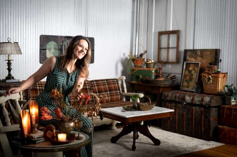 Smiling female food photographer in her studio space filled with picturesque antique props and furniture. 