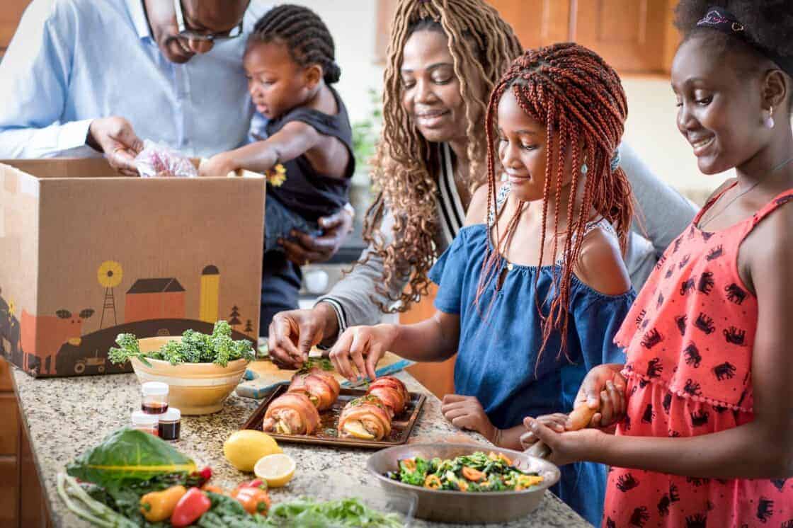 Family around a kitchen island preparing a meal from a meal kit box