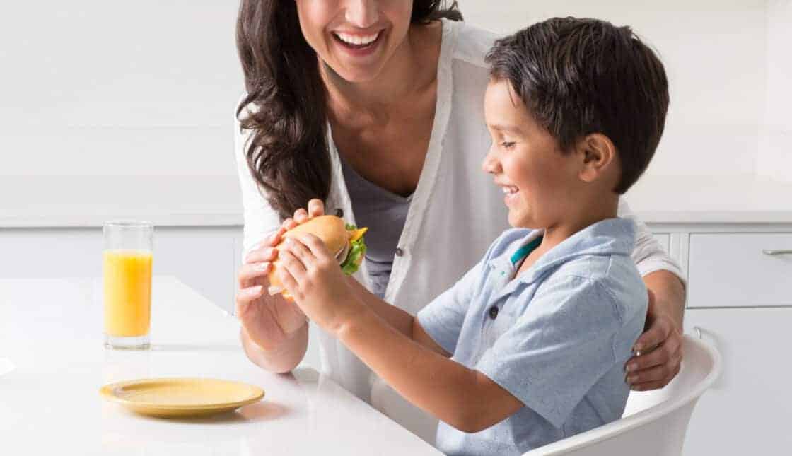 Mom serving her young son dinner in a bright white kitchen