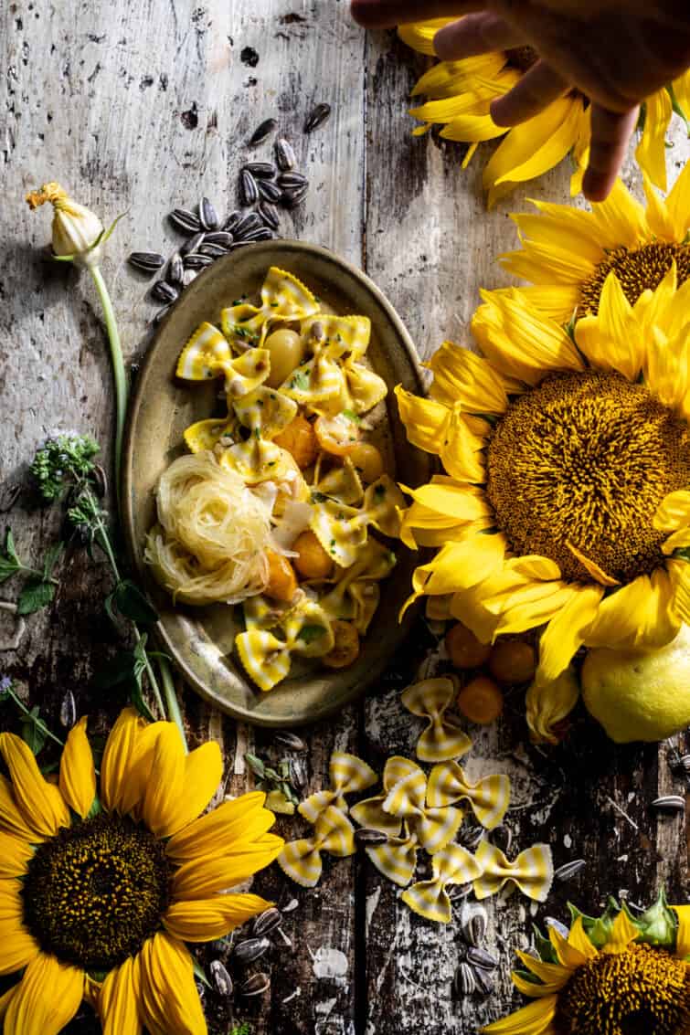 Overhead shot of sunflower lemon pasta with food stylist hand at the top, adjusting the food. 