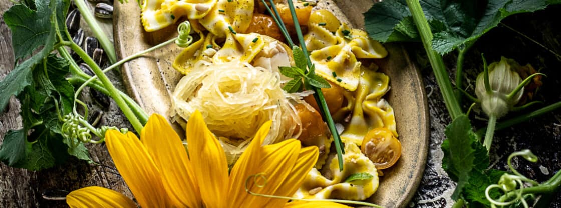 Overhead shot of sunflower lemon pasta in rustic dish surrounded by fresh sunflowers. 