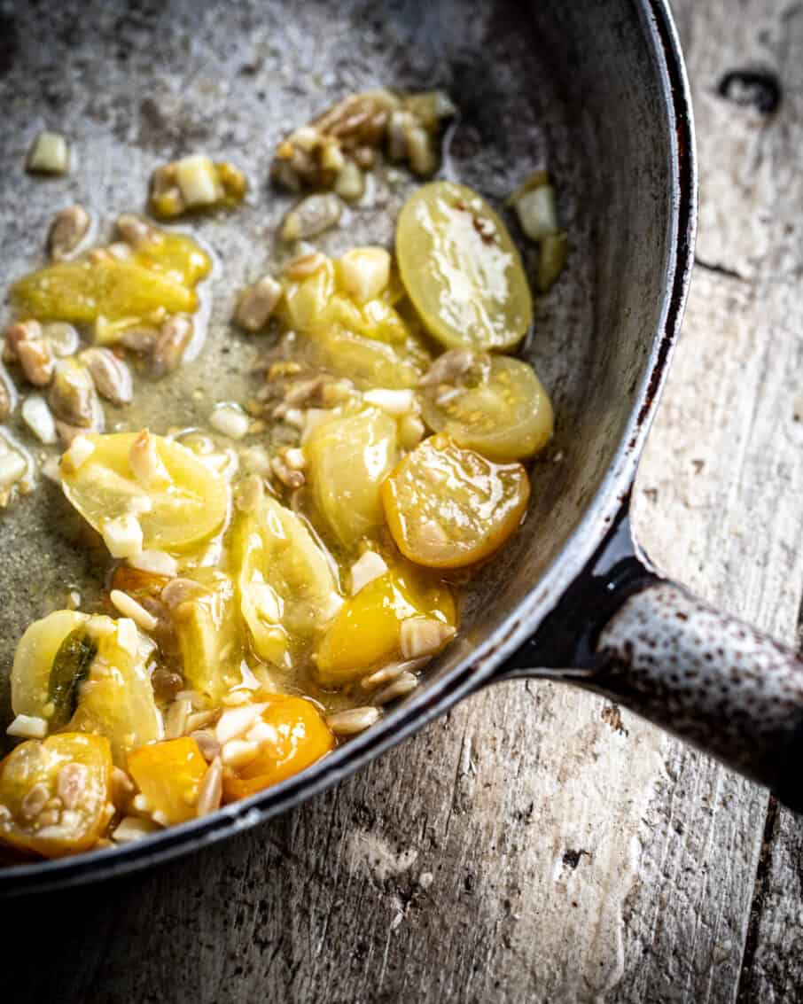 Close up of halved yellow cherry tomatoes in a pan with garlic and butter. 