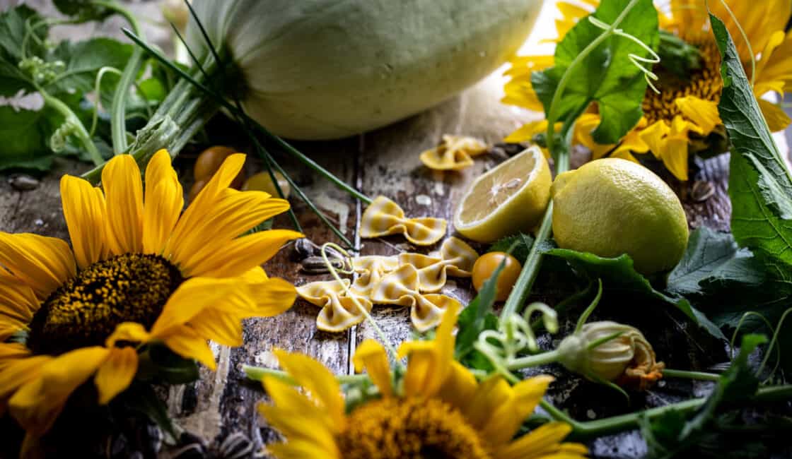 Fresh recipe ingredients gathered on a rustic surface with large sunflowers and a spaghetti squash. 