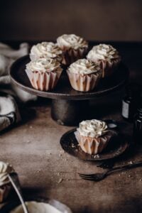 White frosted cupcakes on black cake stand in moody setting.