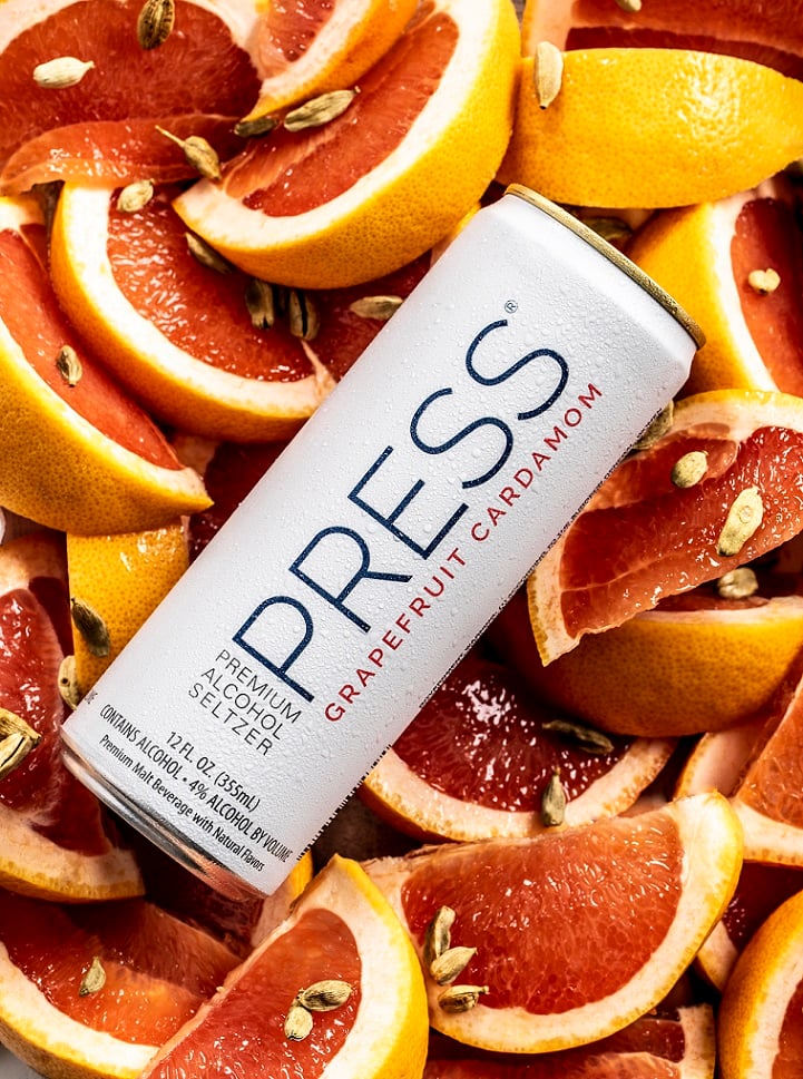 Can of Press hard seltzer on bed of sliced grapefruit and cardamom, cold can photography